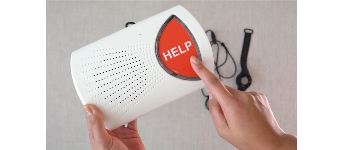 Bay Alarm Medical SOS Home base unit with its help button being pressed, neck pendant and wrist button beside it